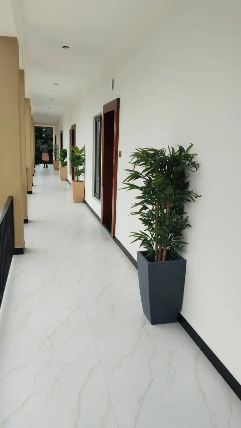 Marble-floored corridor lined with planters leading to guest rooms at Sai Grand Resorts, Kumbakarai