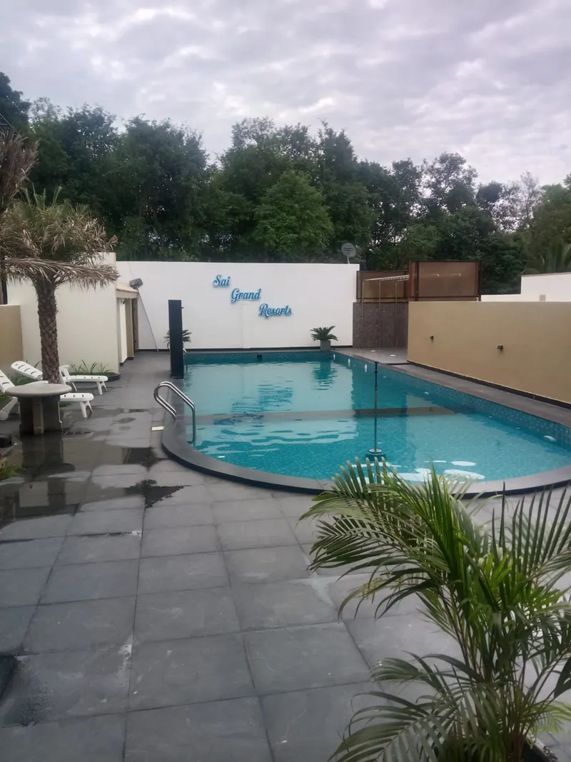 Swimming pool with loungers and palms in daylight at Sai Grand Resorts, Kumbakarai